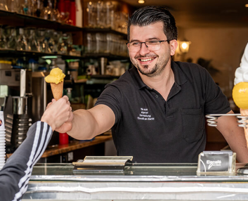 Tim Gafur, der Inhaber des Eiscafés am Markt in Herzogenaurach, reicht eine Tüte Eis über die Theke