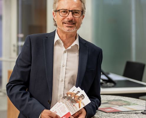 Bernd Dittrich von der Sparkasse Herzogenaurach, Sponsor der Initiative herzoBotschafter:innen steht in der Sparkasse an einem Tresen gelehnt und hat Prospekte in der Hand
