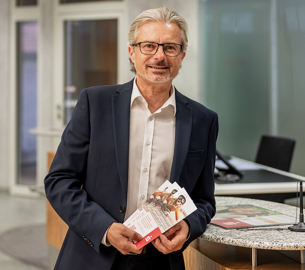 Bernd Dittrich von der Sparkasse Herzogenaurach, Sponsor der Initiative herzoBotschafter:innen steht in der Sparkasse an einem Tresen gelehnt und hat Prospekte in der Hand